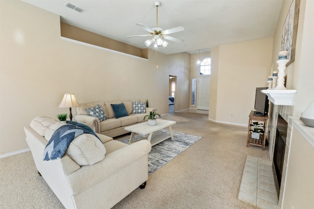 living area with baseboards, visible vents, a fireplace with flush hearth, ceiling fan, and light colored carpet