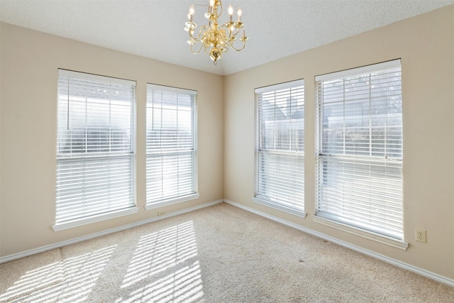 empty room featuring a textured ceiling, a chandelier, and carpet