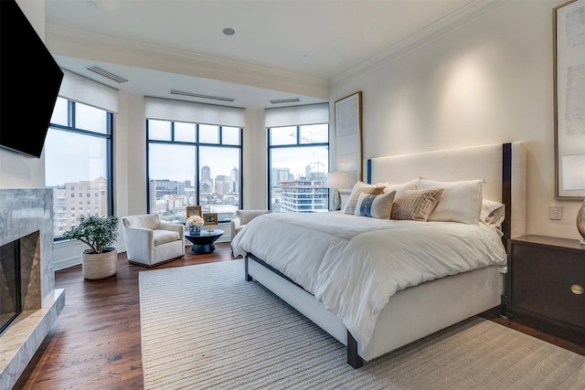 bedroom featuring visible vents, a high end fireplace, wood finished floors, a view of city, and ornamental molding