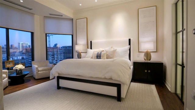 bedroom featuring crown molding, a view of city, baseboards, wood finished floors, and visible vents