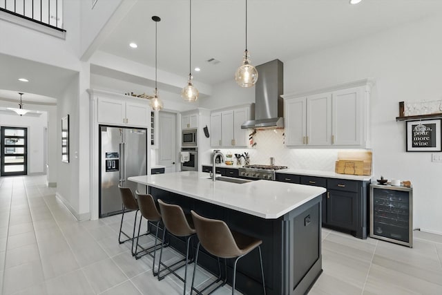 kitchen featuring a sink, stainless steel appliances, wine cooler, wall chimney range hood, and backsplash