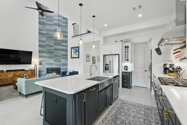 kitchen featuring visible vents, a sink, a large fireplace, appliances with stainless steel finishes, and wall chimney range hood