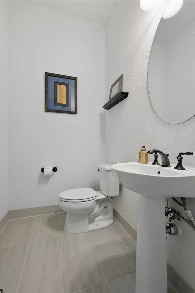 half bath with tile patterned floors, toilet, and baseboards