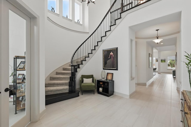 entryway with light tile patterned floors, baseboards, stairs, and a towering ceiling