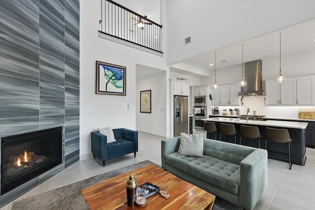 living area featuring a high ceiling, light tile patterned flooring, a fireplace, and visible vents