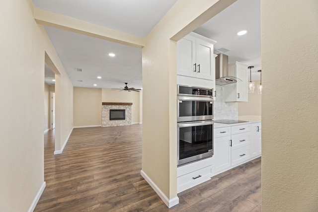 kitchen featuring dark wood-type flooring, ceiling fan, black electric stovetop, double oven, and wall chimney exhaust hood