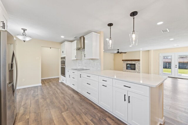 kitchen featuring visible vents, open floor plan, stainless steel appliances, a peninsula, and wall chimney range hood