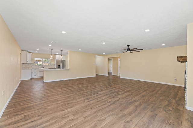 unfurnished living room featuring a sink, baseboards, a ceiling fan, and wood finished floors