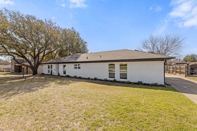 exterior space featuring a yard, brick siding, roof with shingles, and fence