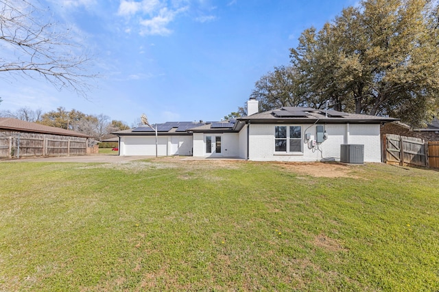 back of property featuring central AC unit, solar panels, a garage, fence private yard, and a lawn