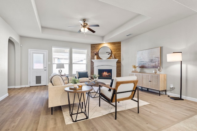 living room featuring light wood-type flooring, a raised ceiling, ceiling fan, and a fireplace