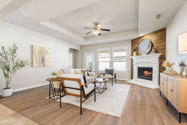 living area with a tray ceiling, a ceiling fan, visible vents, and light wood-type flooring