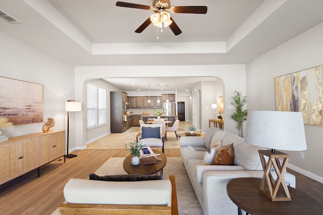 living room with visible vents, arched walkways, a raised ceiling, and light wood-style flooring