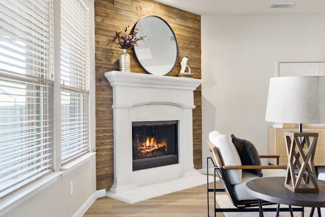 interior space with visible vents, a warm lit fireplace, wooden walls, and wood finished floors