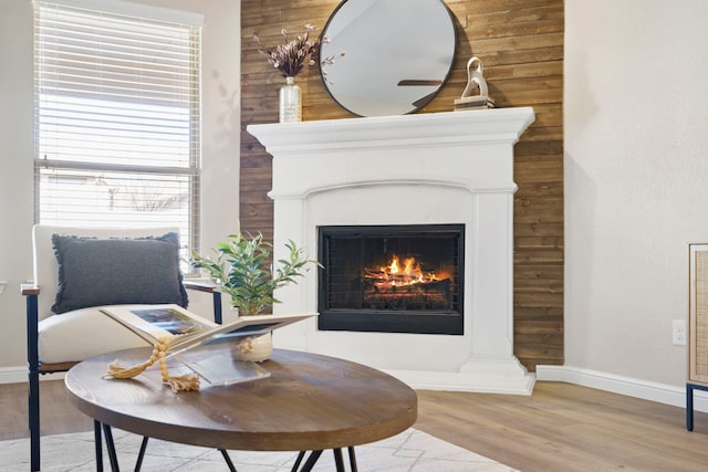 living area with a warm lit fireplace, baseboards, and wood finished floors