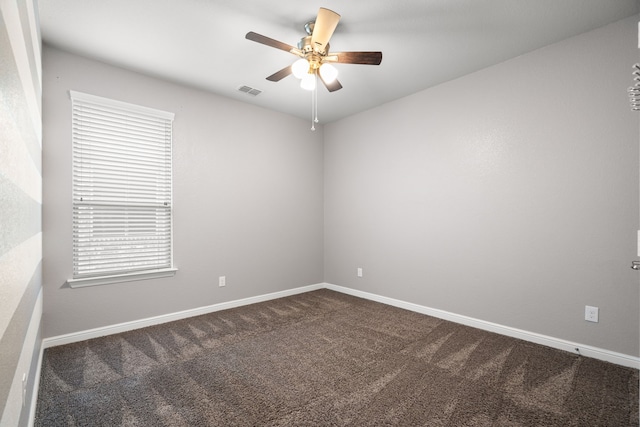 empty room featuring dark colored carpet, visible vents, baseboards, and a ceiling fan