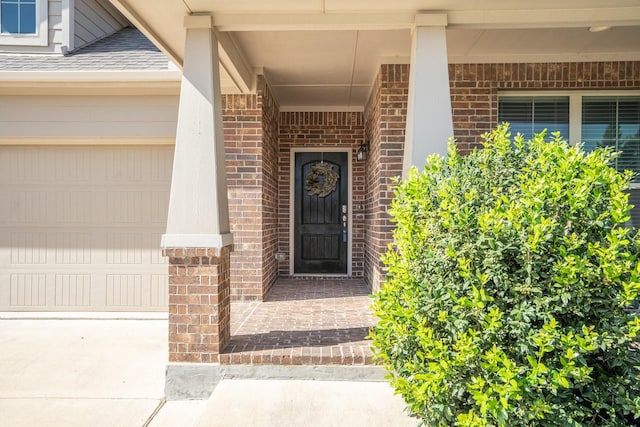 entrance to property with brick siding, concrete driveway, a garage, and roof with shingles