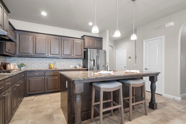 kitchen with stainless steel fridge with ice dispenser, light stone counters, decorative backsplash, a kitchen breakfast bar, and arched walkways