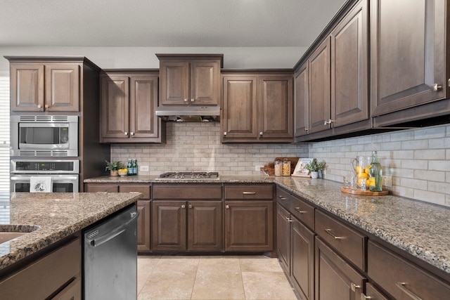 kitchen featuring under cabinet range hood, appliances with stainless steel finishes, tasteful backsplash, and light stone countertops