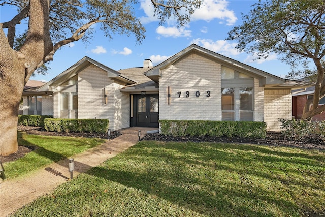 mid-century home with brick siding, a chimney, and a front lawn