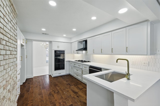 kitchen with dobule oven black, a sink, gas stovetop, a peninsula, and wall chimney exhaust hood