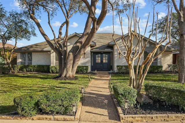 view of front of house featuring french doors, brick siding, and a front lawn