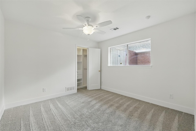 unfurnished bedroom with visible vents, baseboards, a walk in closet, and carpet flooring