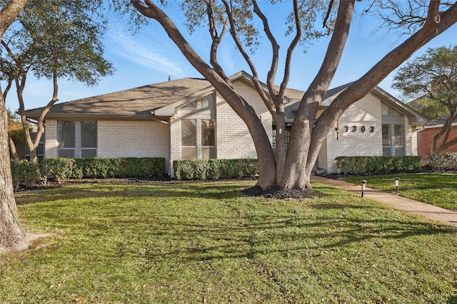 view of front facade featuring a front lawn, brick siding, and a shingled roof