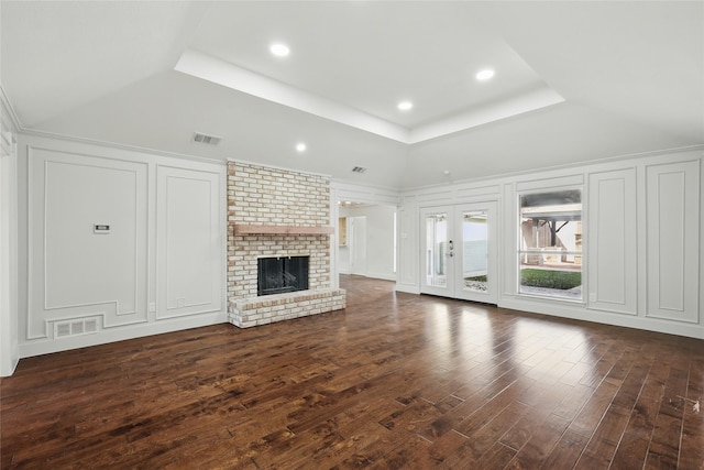 unfurnished living room with a tray ceiling, visible vents, and a decorative wall