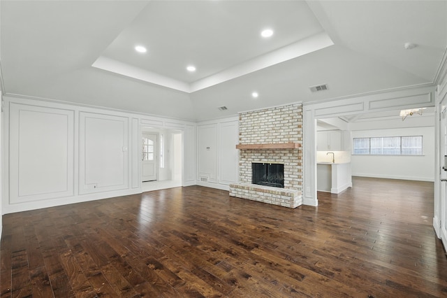 unfurnished living room featuring visible vents, dark wood finished floors, a fireplace, a decorative wall, and a raised ceiling