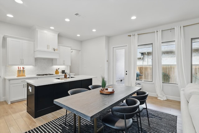 kitchen with visible vents, a center island with sink, a sink, light wood-style floors, and light countertops