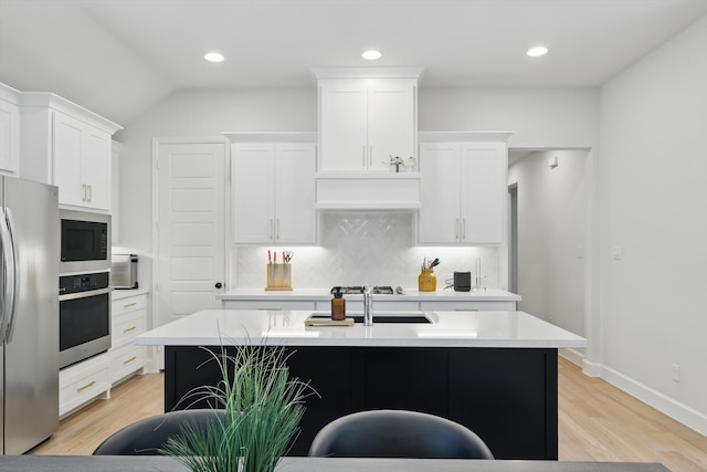 kitchen featuring stainless steel appliances, a center island with sink, white cabinets, and light countertops