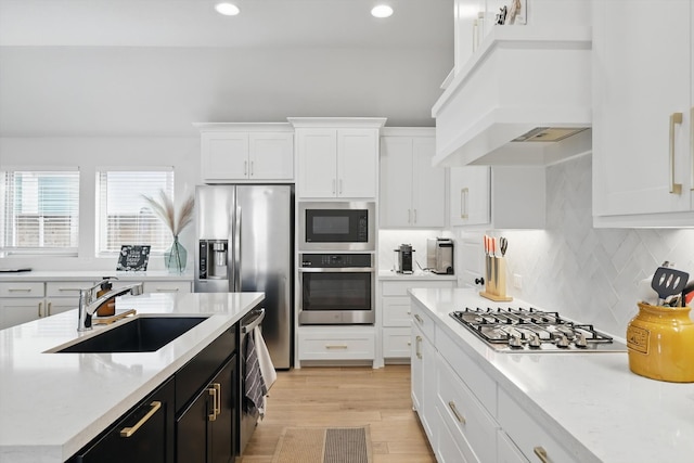 kitchen with custom range hood, a sink, appliances with stainless steel finishes, white cabinets, and dark cabinets