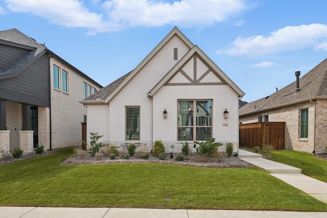 tudor home with brick siding, a front lawn, and fence