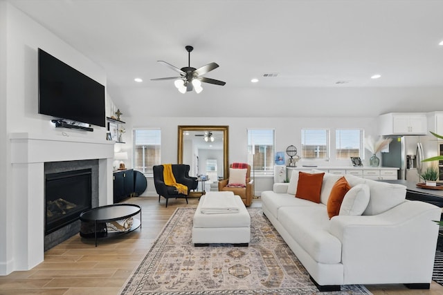 living room featuring visible vents, light wood-style floors, a fireplace, a healthy amount of sunlight, and ceiling fan