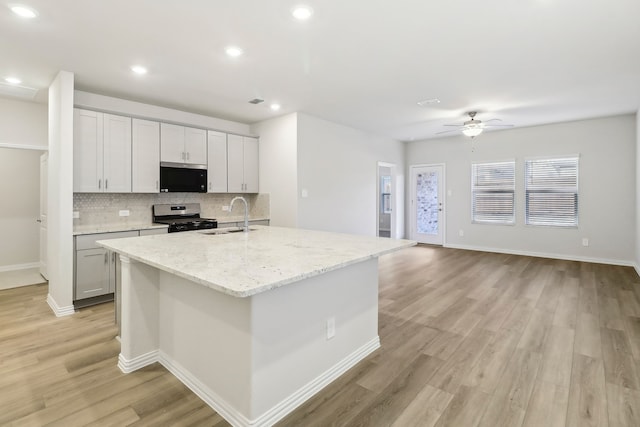 kitchen with stainless steel gas range oven, light wood finished floors, tasteful backsplash, ceiling fan, and a sink