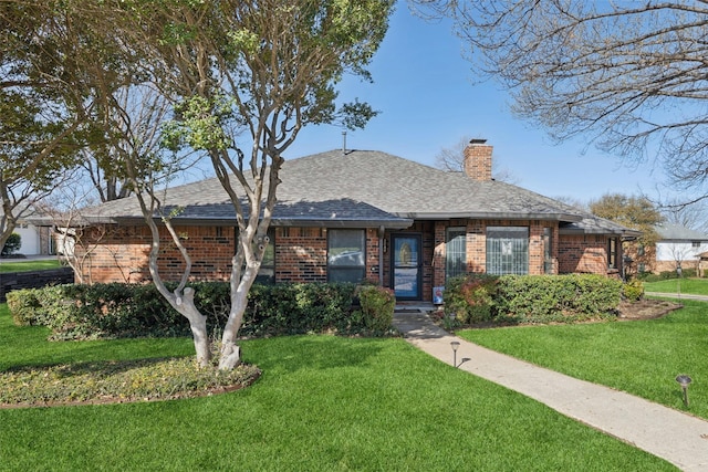 ranch-style house featuring brick siding, a chimney, a front yard, and a shingled roof