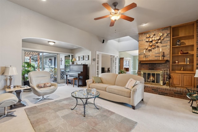 carpeted living area with arched walkways, a brick fireplace, and a ceiling fan