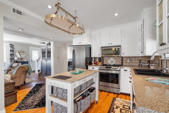 kitchen with a sink, appliances with stainless steel finishes, white cabinets, crown molding, and light wood finished floors