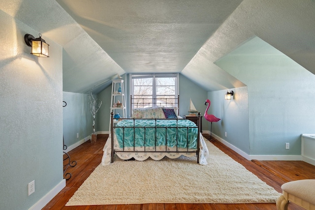 bedroom featuring vaulted ceiling, wood finished floors, baseboards, and a textured ceiling