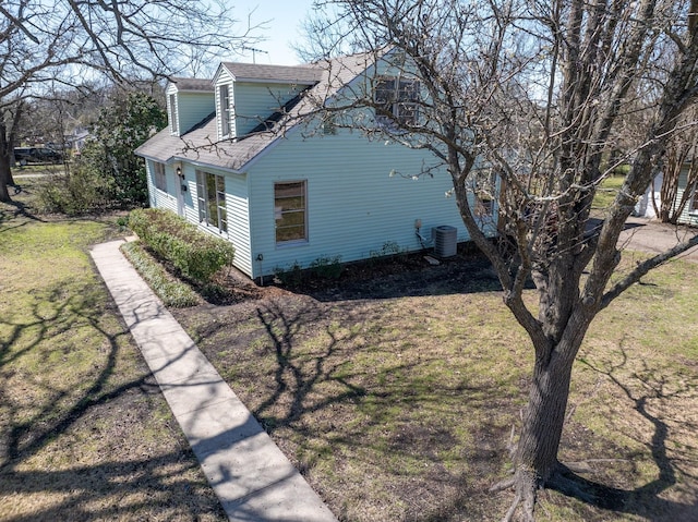 view of side of home featuring a yard, central AC, and a shingled roof