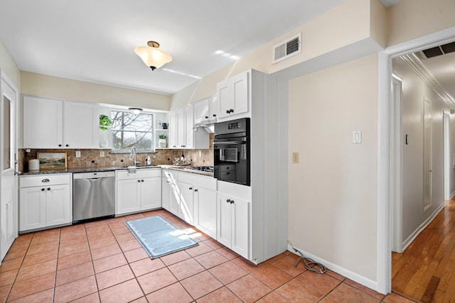 kitchen with backsplash, light tile patterned floors, stainless steel appliances, white cabinetry, and a sink