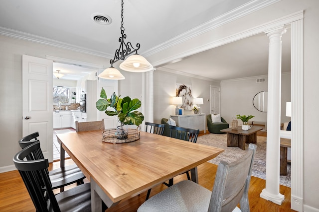 dining room with visible vents, light wood finished floors, ornamental molding, and ornate columns