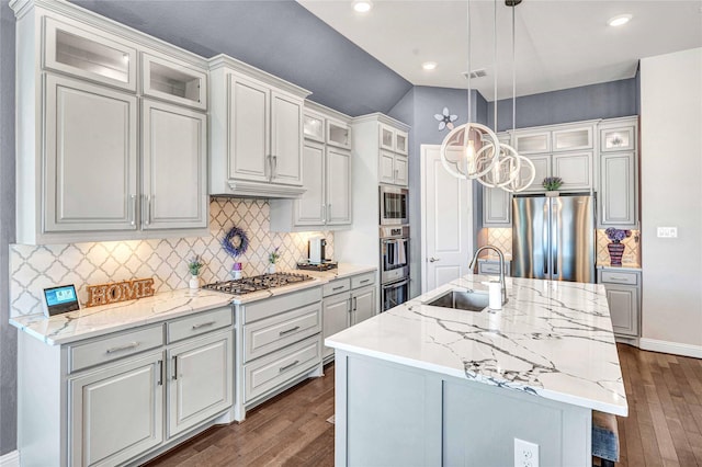 kitchen featuring a sink, dark wood-type flooring, decorative light fixtures, stainless steel appliances, and a kitchen island with sink