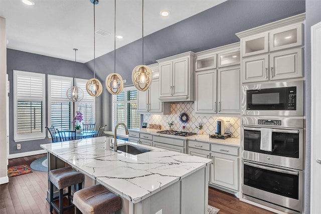 kitchen with dark wood-type flooring, an island with sink, decorative backsplash, stainless steel appliances, and a sink