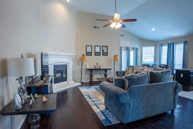 living area with visible vents, high vaulted ceiling, a ceiling fan, a glass covered fireplace, and wood finished floors