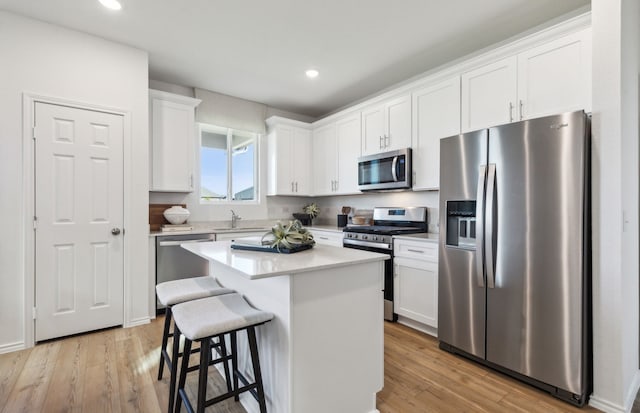 kitchen featuring a breakfast bar area, a sink, stainless steel appliances, white cabinets, and a center island