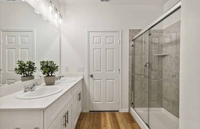 full bath with a shower stall, wood finished floors, double vanity, and a sink