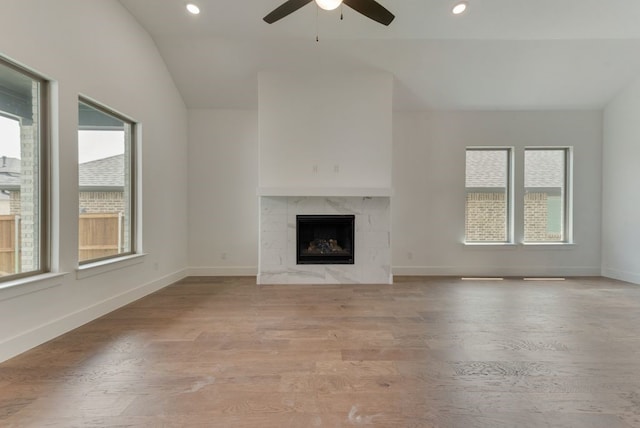 unfurnished living room with baseboards, lofted ceiling, a high end fireplace, ceiling fan, and light wood-type flooring