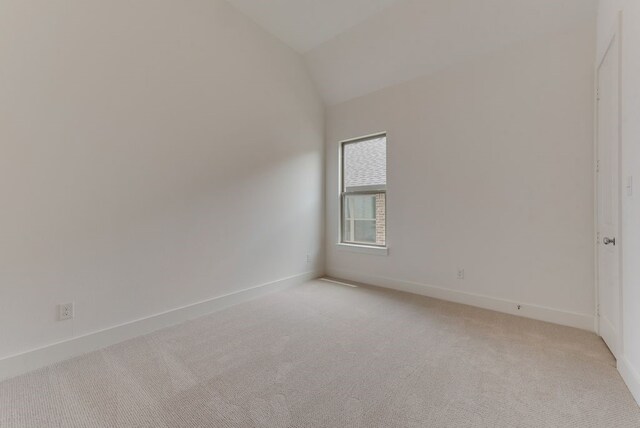 spare room featuring lofted ceiling, light colored carpet, and baseboards